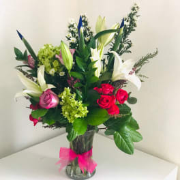 Mixed bouquet of lilies, roses, and hydrangea in a glass vase with a pink ribbon