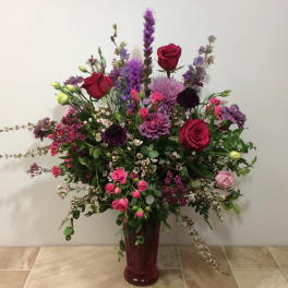 Tall bouquet of red, pink, and purple flowers in a red vase