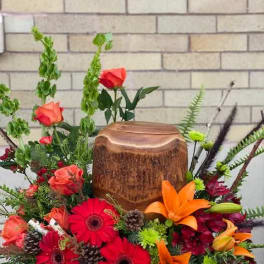 Bright mixed floral arrangement with roses, gerbera daisies, and lilies around a wooden urn