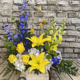 Yellow lilies and roses with blue flowers in a wooden box