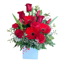 Red roses and gerbera daisies in a blue vase with heart accents