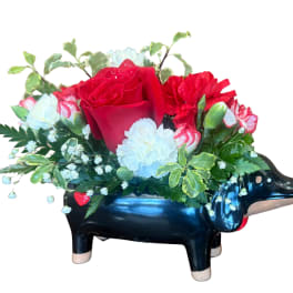 Red rose arrangement in a black dachshund-shaped container