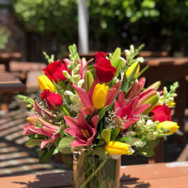 Mixed bouquet of red roses, pink lilies, and yellow tulips in a glass vase