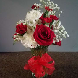 Red and white flower arrangement in a glass vase with a red ribbon