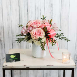 Pink roses and alstroemeria in a white vase with a pink ribbon