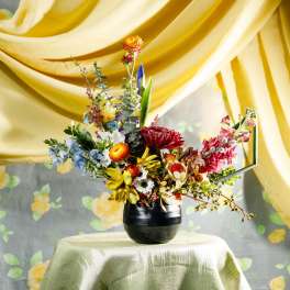 Colorful wildflower-style arrangement in a black vase on a draped table