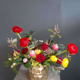 Mixed bouquet of red, pink, and yellow flowers in a gold vase