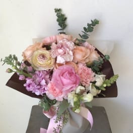 Bouquet of pink, peach, and white flowers wrapped in dark paper with a pink ribbon