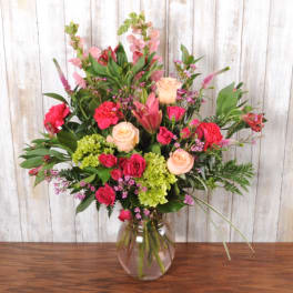 Tall mixed bouquet of pink and peach flowers with green hydrangea in a clear glass vase