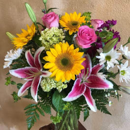 Bouquet of sunflowers, pink roses, lilies, and white daisies in a glass vase