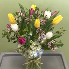 Mixed tulip and hydrangea arrangement with pink filler flowers in a clear glass vase tied with raffia.