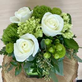White roses and green flowers arranged in a square glass vase