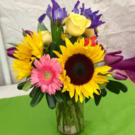 Colorful bouquet with sunflowers, roses, irises, and a gerbera daisy in a glass vase