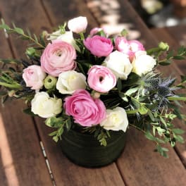 Pink and white ranunculus bouquet in a dark round container