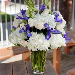White hydrangea and roses with purple irises in a glass vase