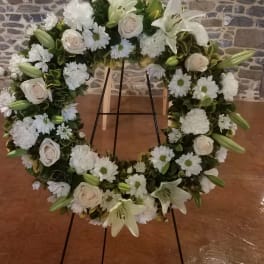 White floral wreath on a stand with lilies, roses, and daisies