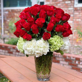 Red roses and white hydrangeas arranged in a clear glass vase