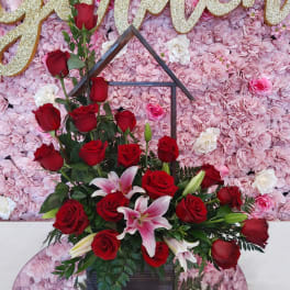 Red roses and lilies in a black house-shaped stand before a pink floral wall