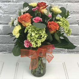 Bouquet of orange roses, pink carnations, and yellow blooms in a glass vase