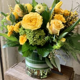 Yellow roses and green blooms arranged in a glass vase