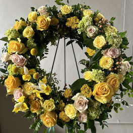 Circular floral wreath with yellow and blush roses on a stand