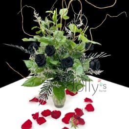 Black roses in a glass vase with red rose petals around it