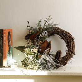 Rustic wreath with pinecones and dried florals beside stacked books