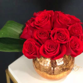 Red roses arranged in a gold vase with a large green leaf