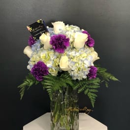 Bouquet of white roses, blue hydrangeas, and purple carnations in a glass vase