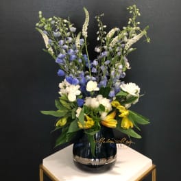 Tall mixed bouquet in a dark glass vase with blue, white, and yellow flowers