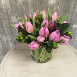 Pink tulips arranged in a clear glass vase with green berries