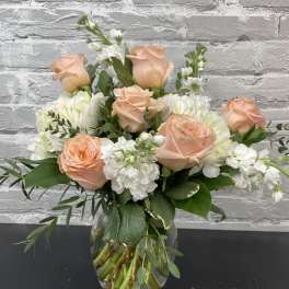 Peach roses and white flowers arranged in a clear glass vase