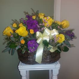Basket arrangement of yellow roses and purple flowers with a cream ribbon
