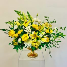 Yellow and white floral arrangement in a gold pedestal vase