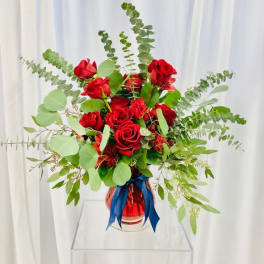 Red roses in a glass vase with blue ribbon and airy greenery