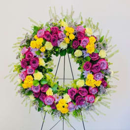 Circular floral wreath of pink, purple, and yellow roses on a stand