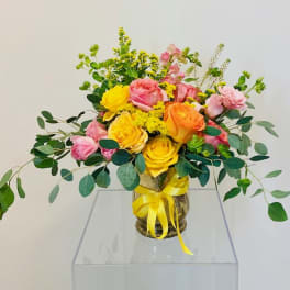 Bouquet of pink and yellow roses in a glass vase with a yellow ribbon