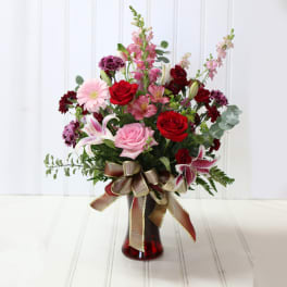 Mixed bouquet of roses, lilies, and pink blooms in a red glass vase