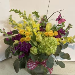 Bouquet of yellow and purple flowers in a glass vase with a pink ribbon