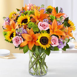 Bouquet of orange lilies, pink roses, and sunflowers in a glass vase