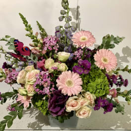Mixed bouquet with pink gerbera daisies, roses, and purple blooms in a vase