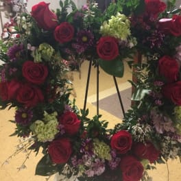 Heart-shaped floral wreath with red roses and purple flowers on an easel