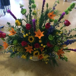 Large mixed flower arrangement in a white basket with orange lilies and red roses