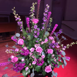 Tall floral arrangement with pink roses and purple flowers in a black stand