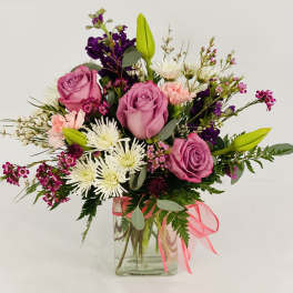 Pink roses and mixed flowers in a clear glass vase with a pink ribbon