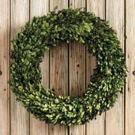 A round green wreath made of dense foliage on a wooden background.