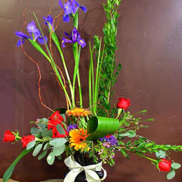 Tall mixed flower arrangement in a black vase with a white ribbon