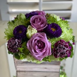 Purple roses and dark blooms arranged in a wooden box