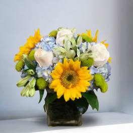 Bouquet of sunflowers, white roses, and blue hydrangeas in a glass vase