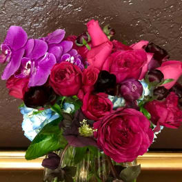 Bouquet of pink roses, purple orchids, and blue hydrangeas in a glass vase